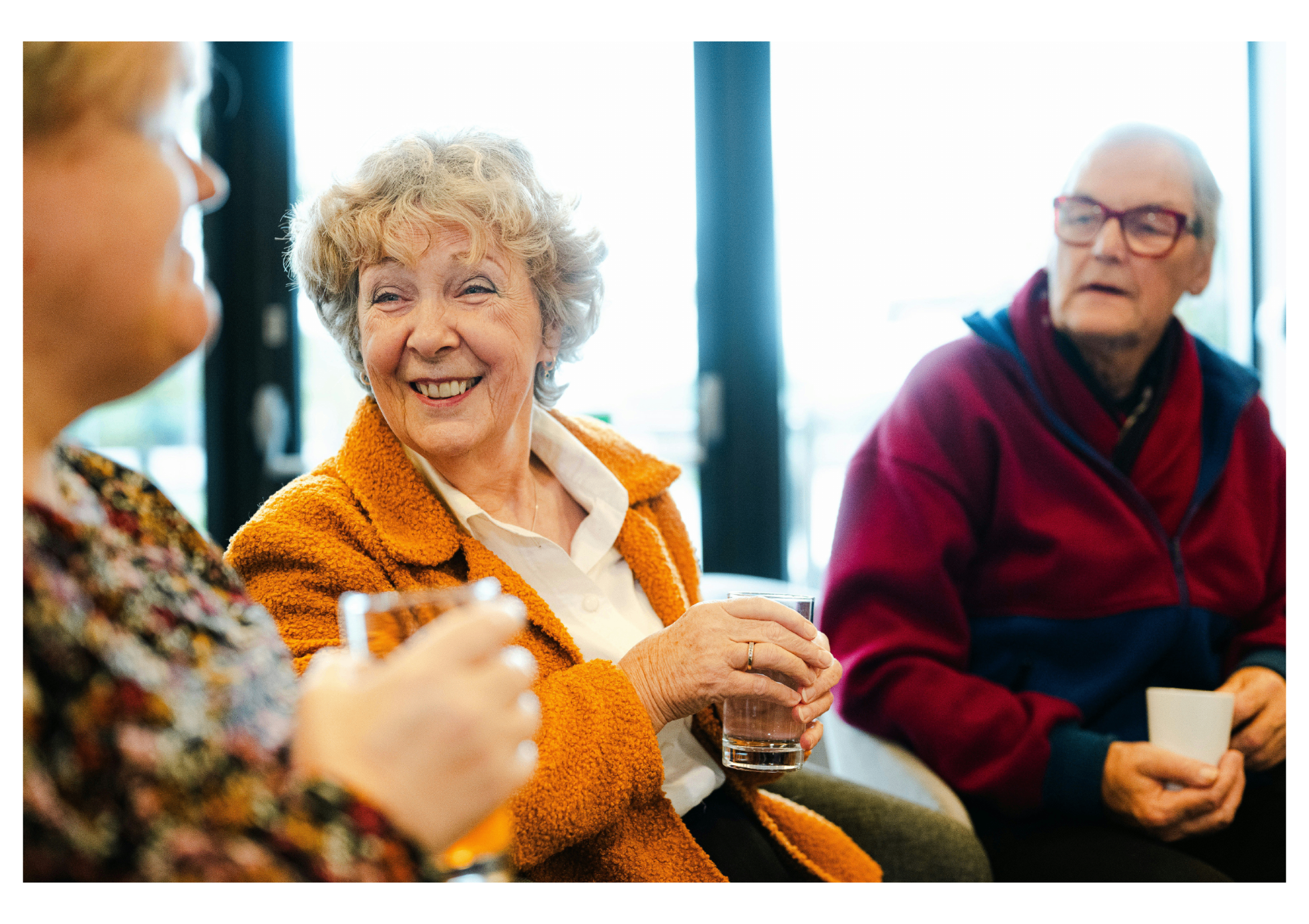 A small group of older friends sitting together, laughing and chatting over drinks